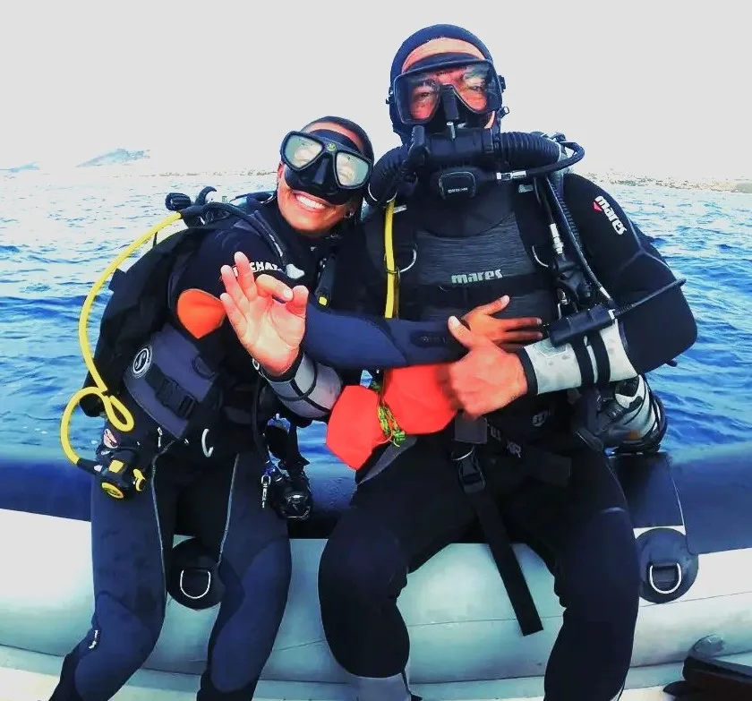 Deux plongeurs souriants en combinaison sur un bateau pneumatique bleu