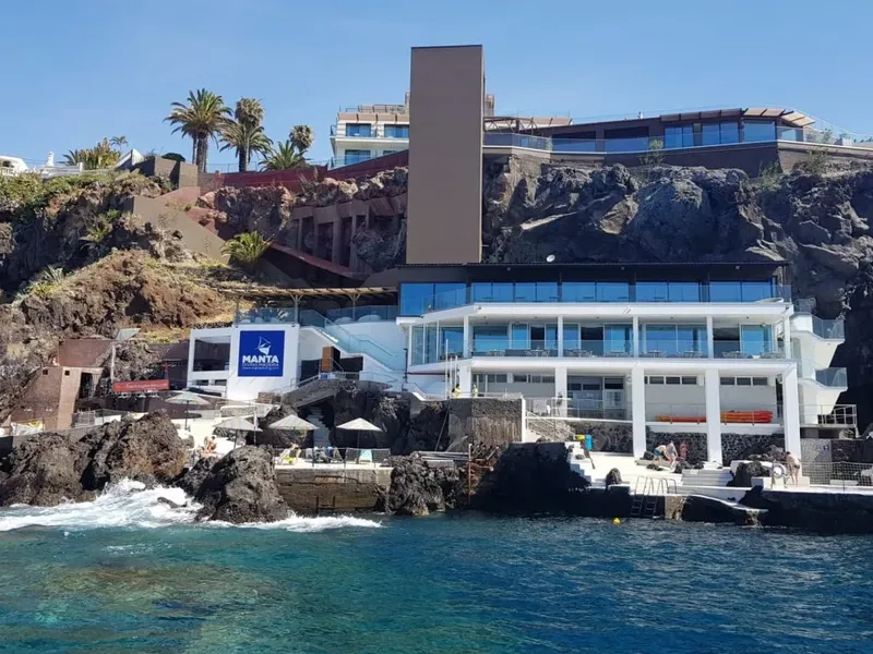 Bâtiment moderne blanc avec logo bleu, au bord de l'océan rocheux