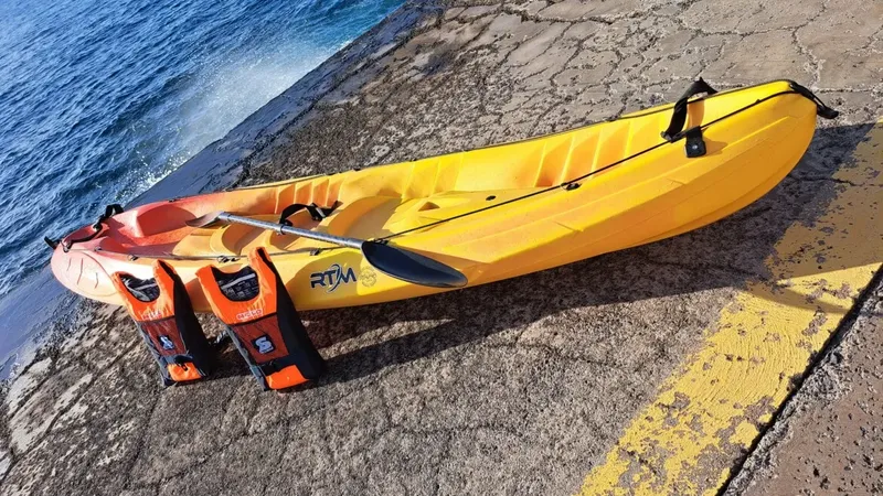 Kayak biplace jaune et orange sur un quai rocheux bleu
