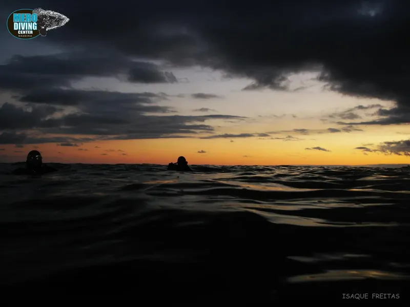 Plongeurs en surface au coucher du soleil, ciel nuageux et mer calme