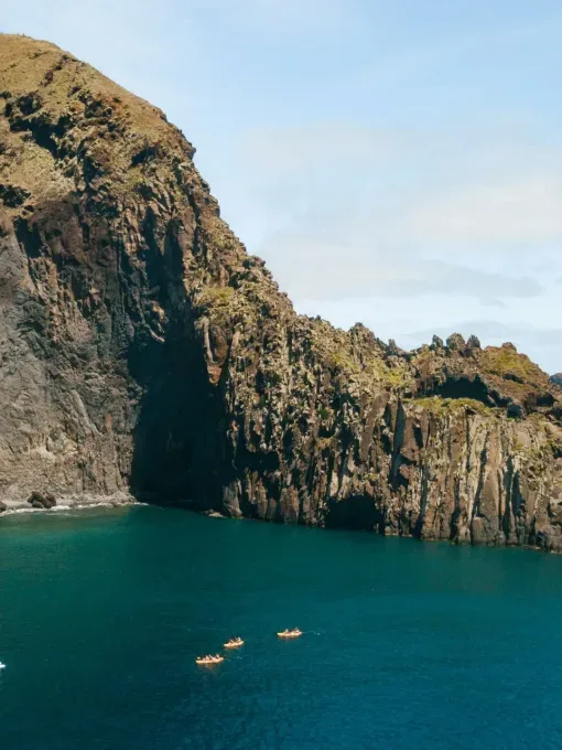 Falaises volcaniques surplombant une mer bleue avec quelques embarcations