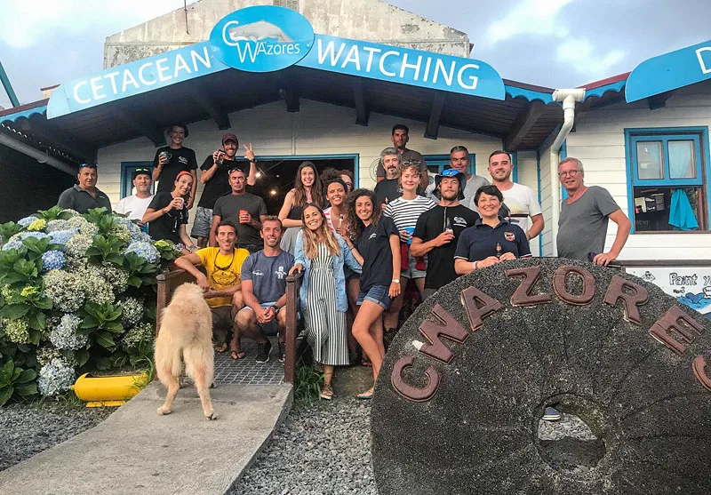 Groupe de personnes souriantes posant devant un bâtiment et une pierre