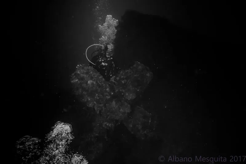 Plongeur en scaphandre noir évolue dans l'obscurité avec des bulles