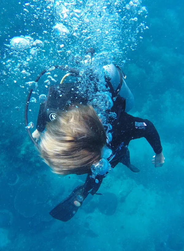 Plongeur en scaphandre noir, cheveux flottants, bulles d'air bleues
