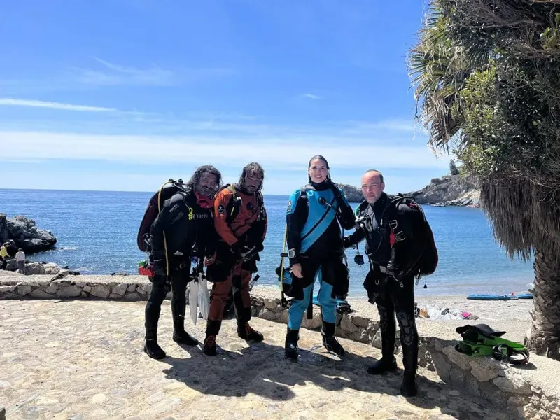 Quatre plongeurs équipés sourient devant la mer et le soleil