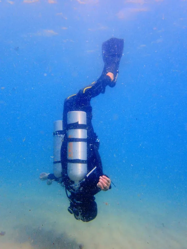Plongeur en combinaison noire nageant verticalement dans une eau bleue claire