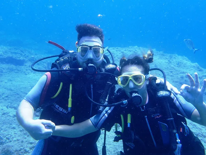 Deux plongeurs souriants, équipés, se regardent dans l'eau bleue