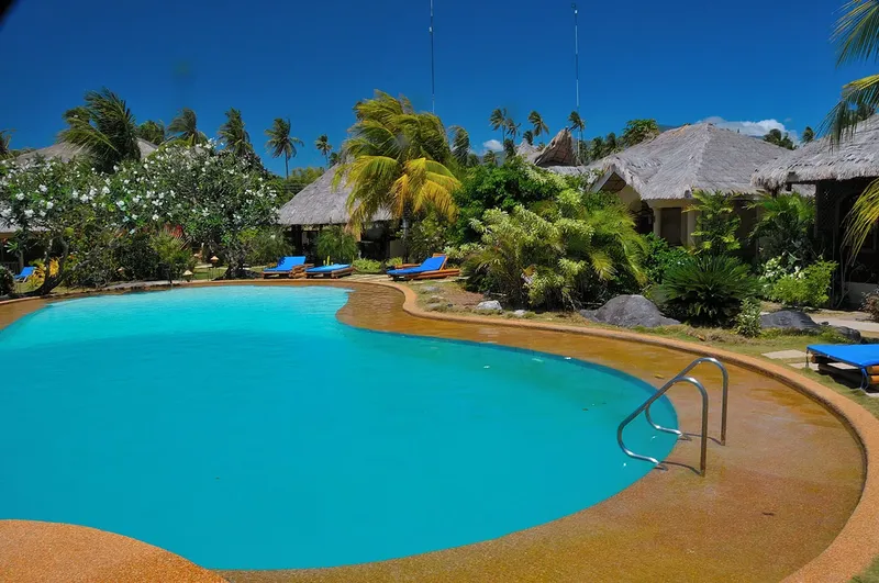 Piscine turquoise entourée de végétation luxuriante et de bâtiments tropicaux