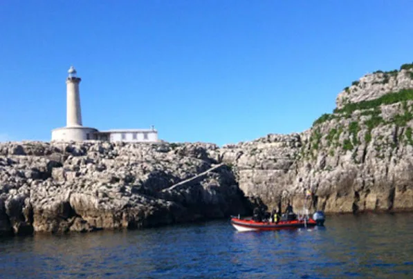 Bateau de plongee avec des personnes près d'une côte rocheuse et d'un phare