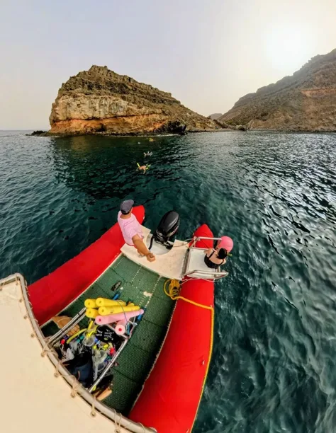 Bateau de plongee rouge avec deux plongeurs et paysage côtier