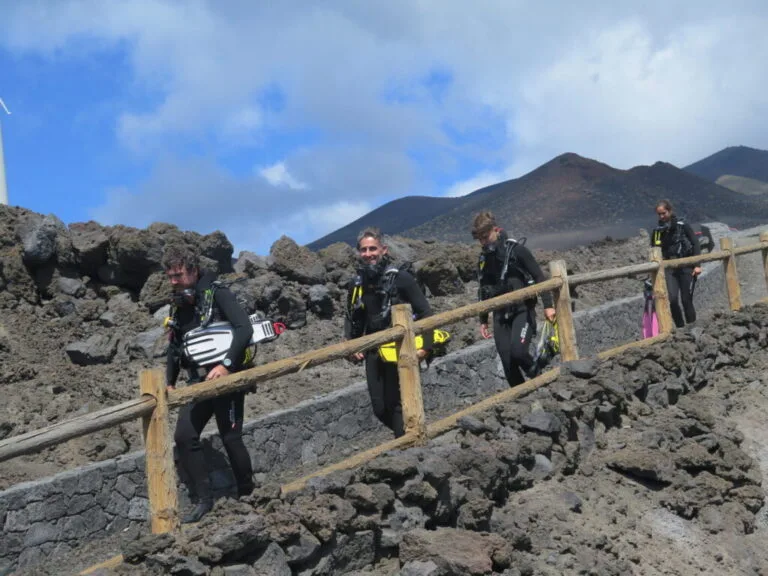 Plongueurs en combinaison marchent sur un terrain volcanique rocheux