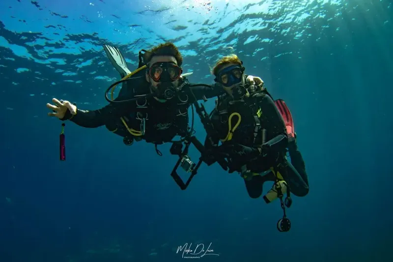 Deux plongeurs souriants évoluent dans une eau bleue claire et ensoleillée