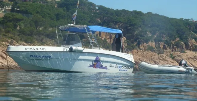 Bateau de plongée amarré près d'une côte rocheuse ensoleillée avec des personnes