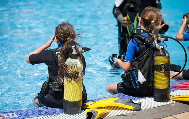Des plongeurs en formation, assis au bord d'une piscine, équipement visible