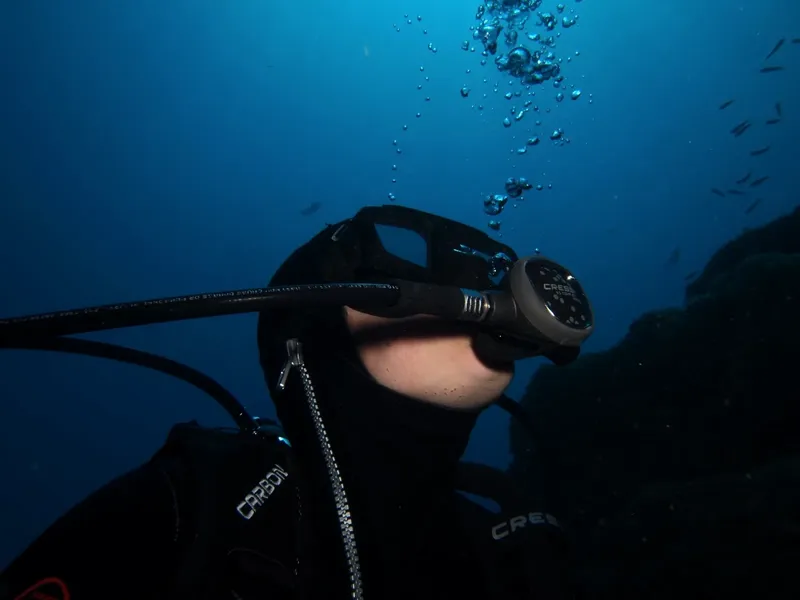 Plongeur en combinaison noire, masque et détendeur dans l'eau bleue