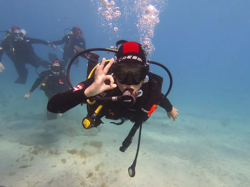 Plongeur souriant avec signe OK, entouré d'autres plongeurs en mer