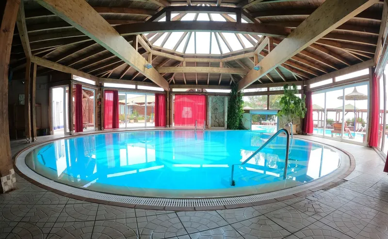 Piscine intérieure circulaire avec structure en bois et grandes baies vitrées
