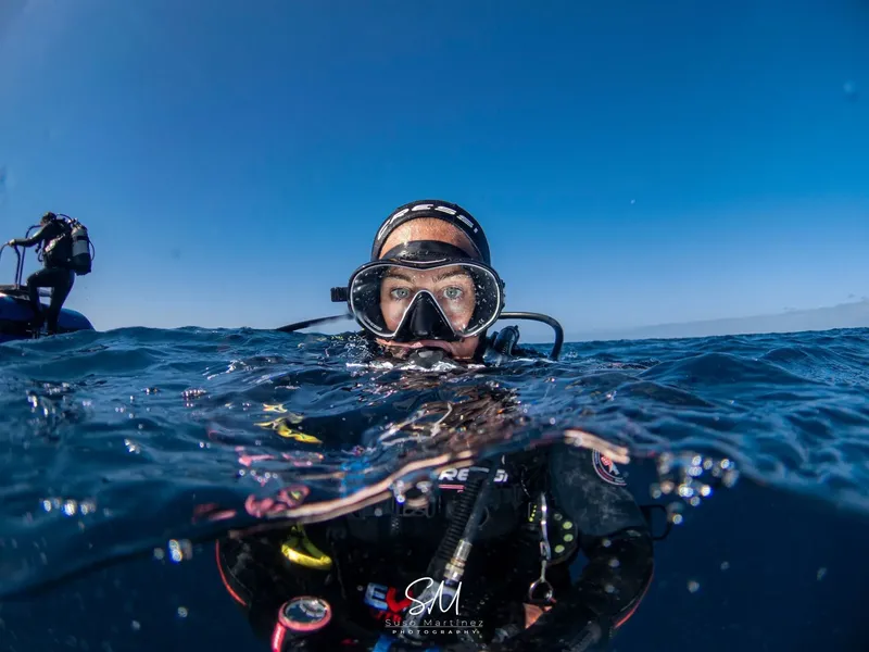 Plongeur regardant la caméra, en surface, avec un bateau en arrière-plan