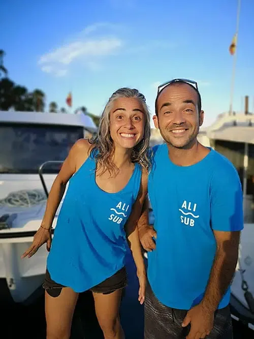 Deux personnes souriantes posent devant des bateaux amarrés au port