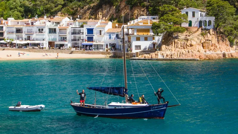 Personnes sur un bateau bleu en mer devant une plage et des maisons