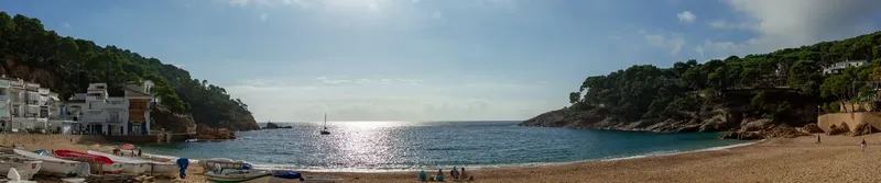 Plage ensoleillée avec quelques personnes et bateaux amarrés au loin