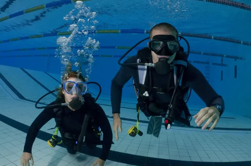 Deux plongeurs en combinaison noire nagent sous l'eau dans une piscine