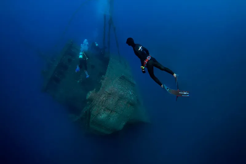 Deux plongeurs explorent une épave sous-marine dans l'eau bleue