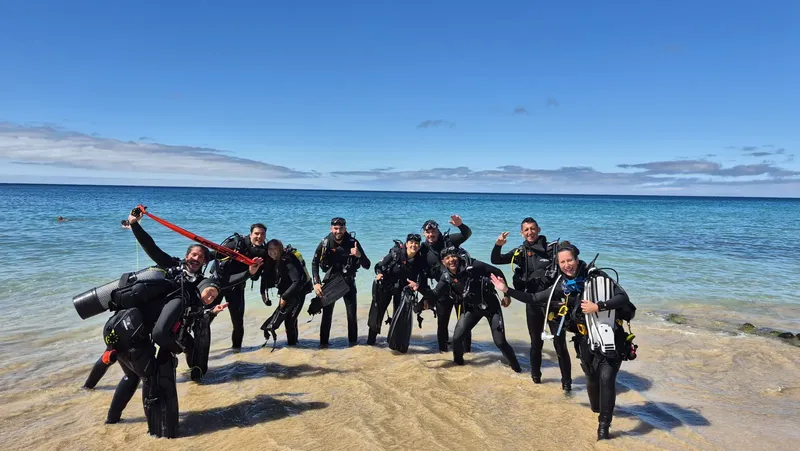 Groupe de plongeurs souriants sur une plage ensoleillée avec équipement