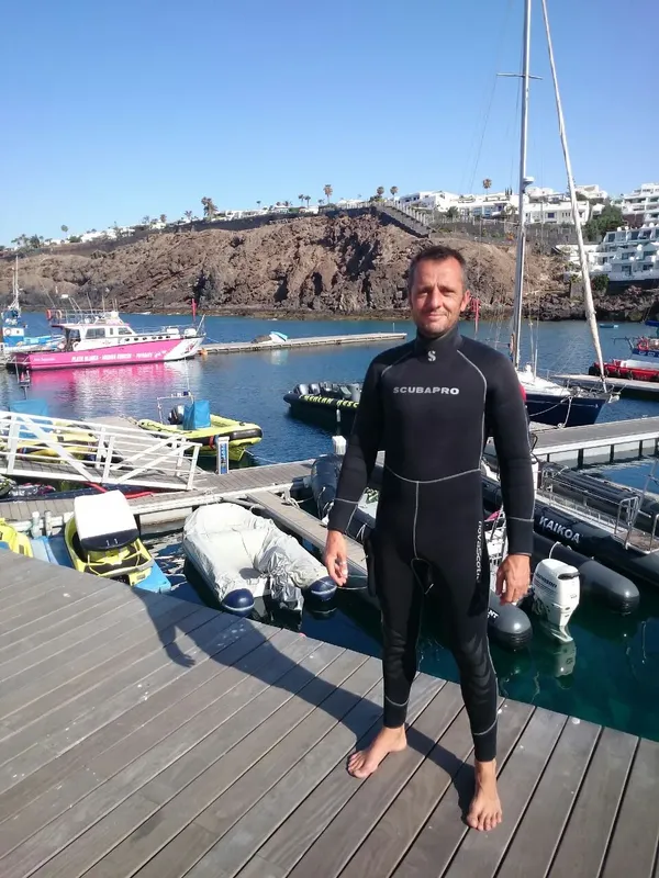 Plongeur en combinaison sur un ponton devant des bateaux amarrés