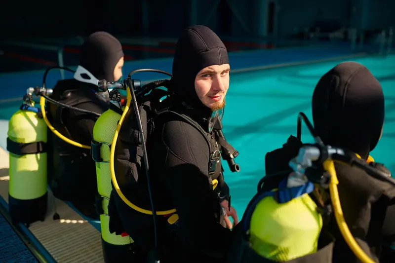 Trois plongeurs équipés près d'une piscine, préparation à une immersion