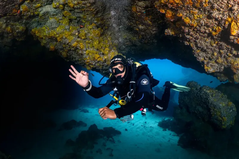 Plongeur souriant faisant un signe de la main dans une grotte sous-marine