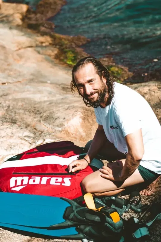 Homme souriant assis à côté d'un sac de plongée Mares orange et blanc