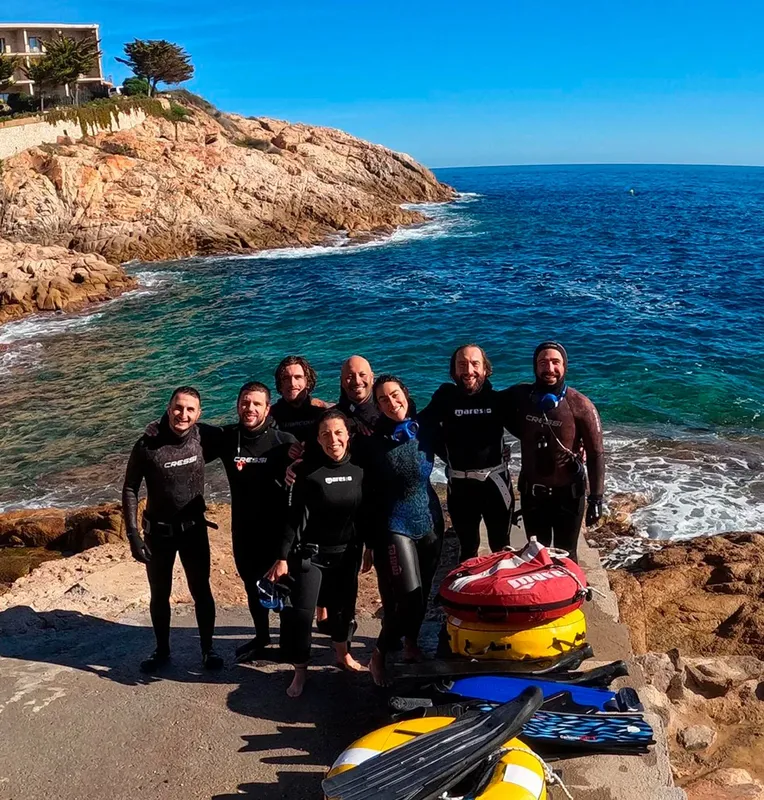 Groupe de plongeurs souriants posant sur un rocher en bord de mer