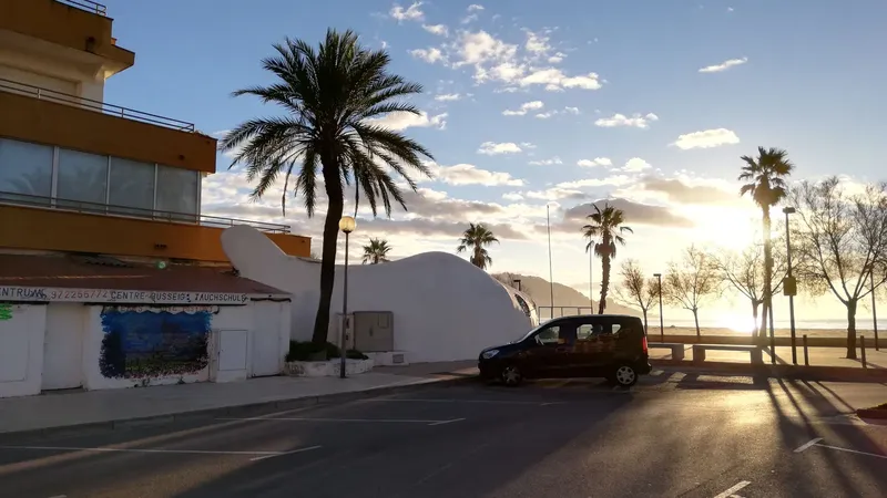 Façade d'un bâtiment jaune et blanc avec palmiers et parking ensoleillé