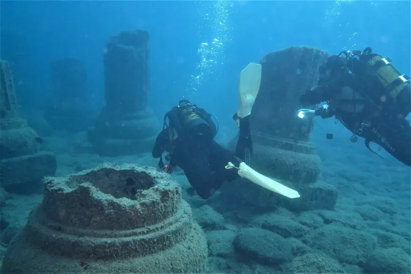 Deux plongeurs explorent des ruines antiques sous l'eau, lumière bleutée