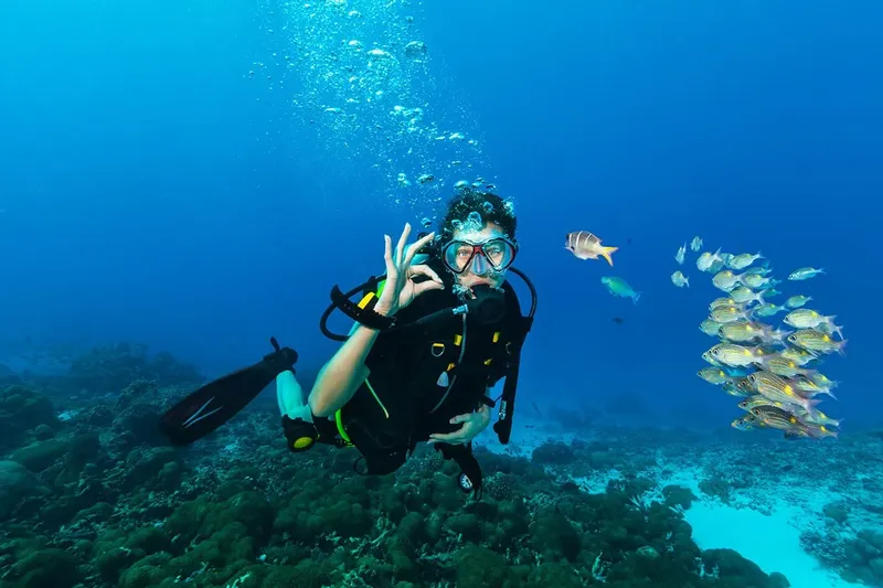 Plongeur souriant avec des poissons tropicaux dans une eau bleue claire