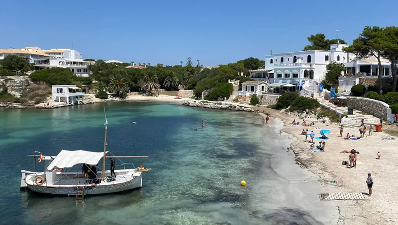 Plage ensoleillée avec un bateau amarré et des personnes se relaxant
