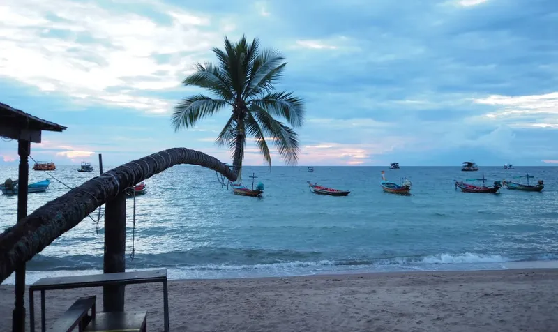Plage tropicale avec plusieurs bateaux de pêche au coucher du soleil