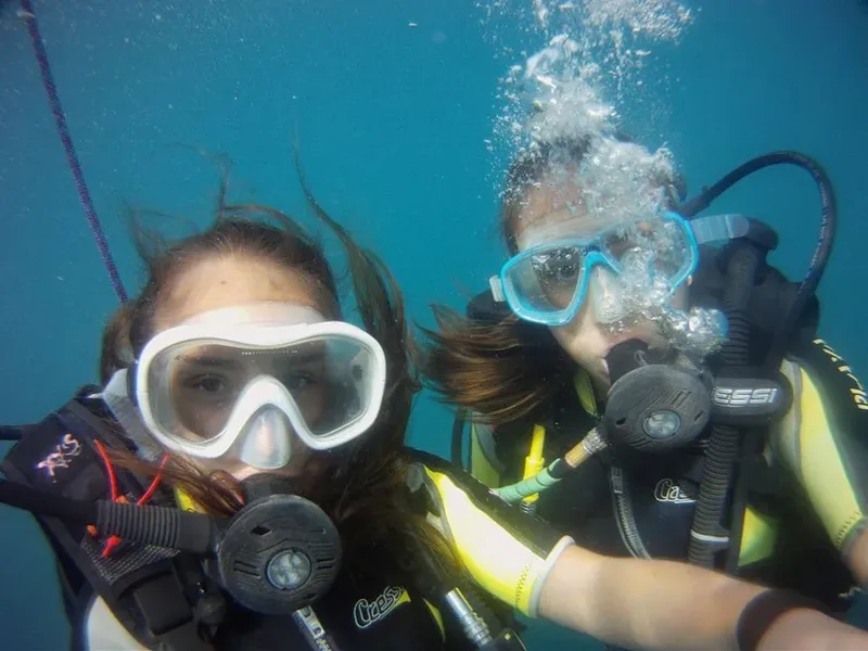 Deux plongeuses souriantes avec leur équipement sous l'eau bleue