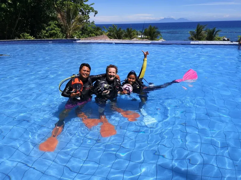Trois plongeurs souriants dans une piscine, équipés de palmes et masques