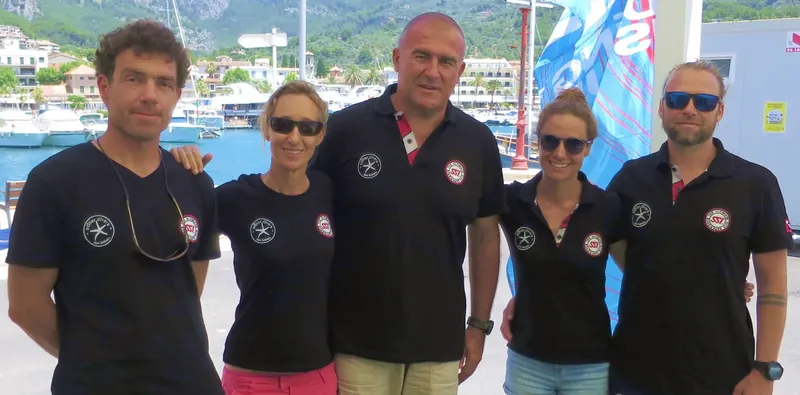 Cinq personnes souriantes posent devant un port de plaisance ensoleillé