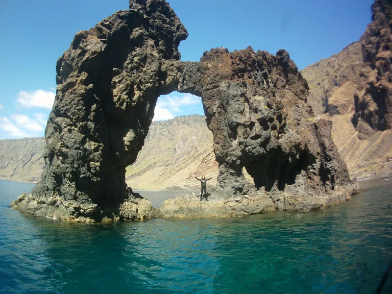 Plongeur bras ouverts devant une arche rocheuse en mer