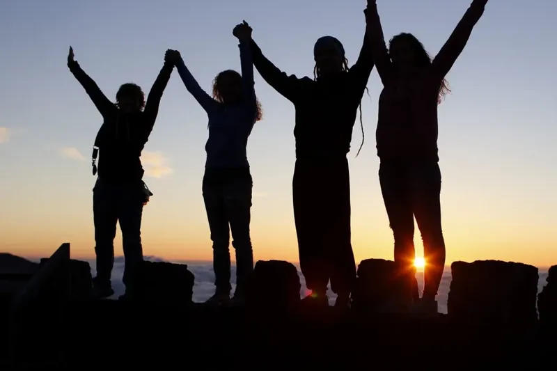 Quatre personnes se tiennent la main, bras levés, au coucher du soleil