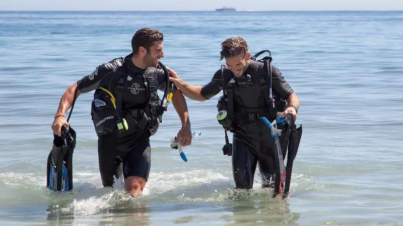Deux plongeurs en combinaison sortent de l'eau sur une plage
