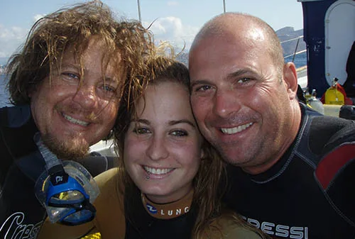 Trois personnes souriantes, portant des équipements de plongée, sur un bateau