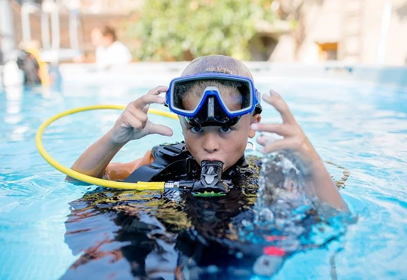 Jeune plongeur ajuste son masque dans une piscine bleu clair