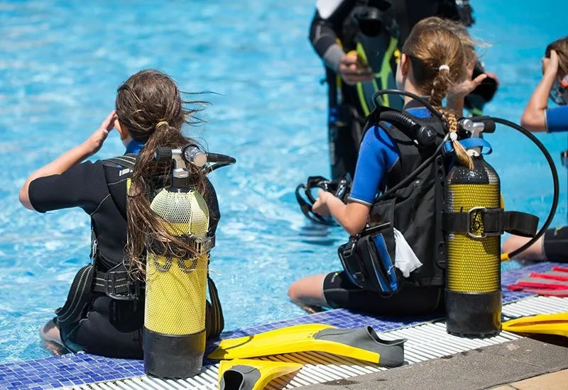 Des plongeurs en formation, équipés, assis au bord d'une piscine