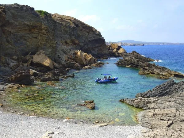 Petit bateau bleu dans une crique rocheuse ensoleillée avec des personnes