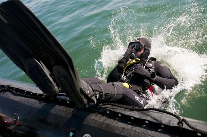 Plongeur en combinaison noire sort de l'eau depuis un bateau pneumatique