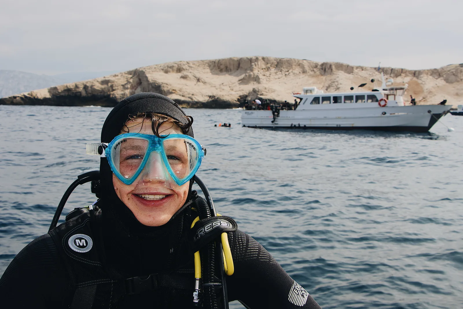 Plongeur souriant en combinaison, bateau de plongée en arrière-plan, mer bleue